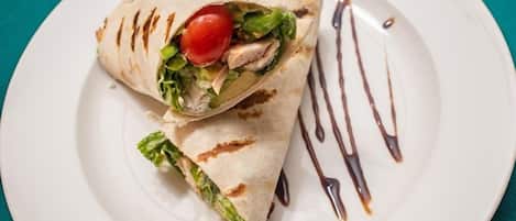 A wrap with lettuce, tomato, and chicken on a white plate with a drizzle of sauce.