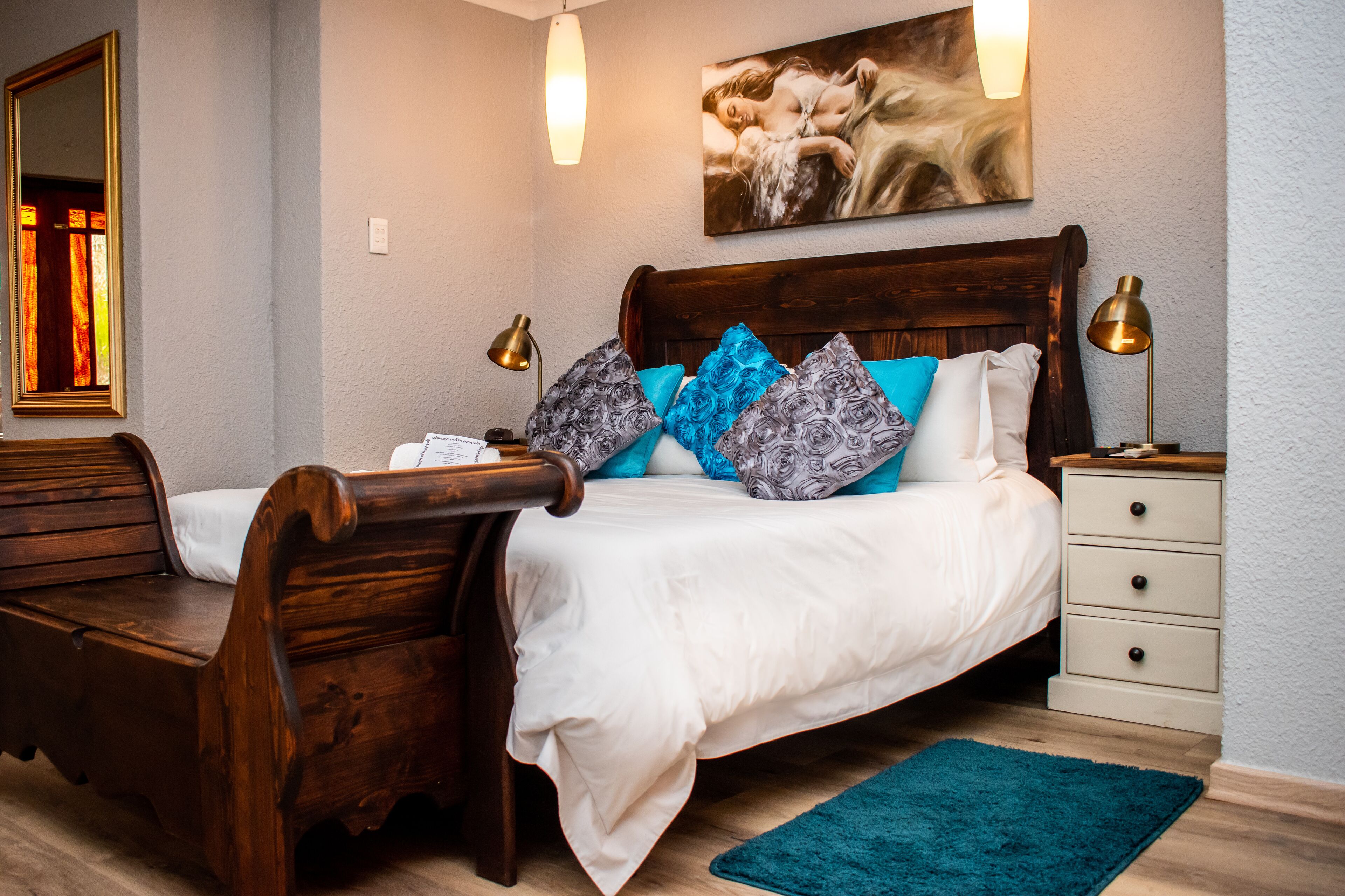 Une chambre à coucher avec un lit en bois, un banc, une table de chevet et un tableau accroché au mur.