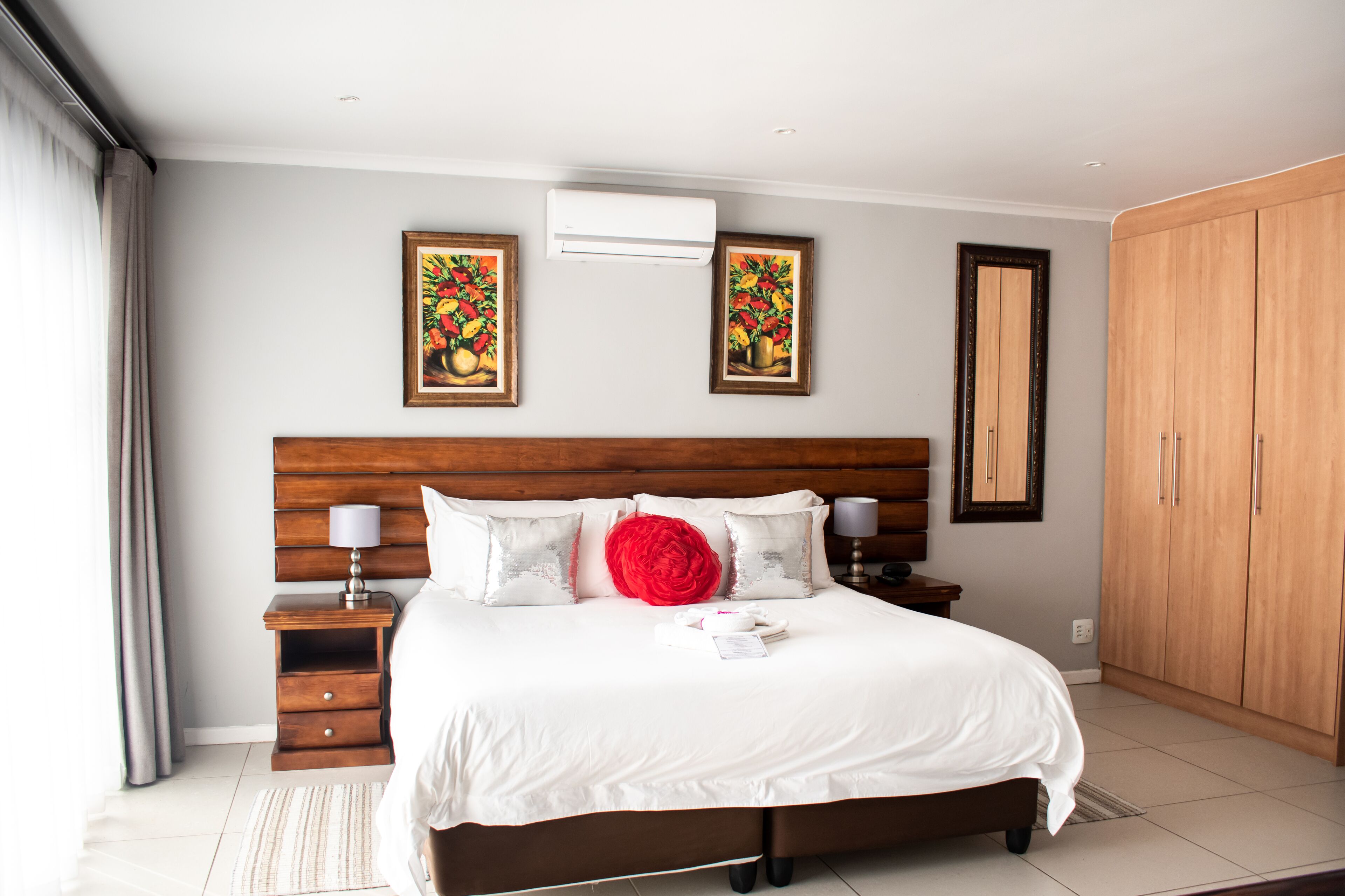 A neatly made bed with white linens, a red decorative pillow, and two framed artworks on the wall.