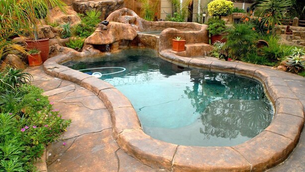 Una piscina con diseño de roca natural, rodeada de plantas y una pequeña cascada.