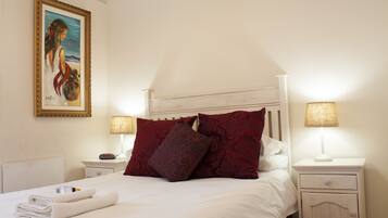 A neatly made bed with white linens and red pillows, two bedside tables with lamps, and a framed painting on the wall.