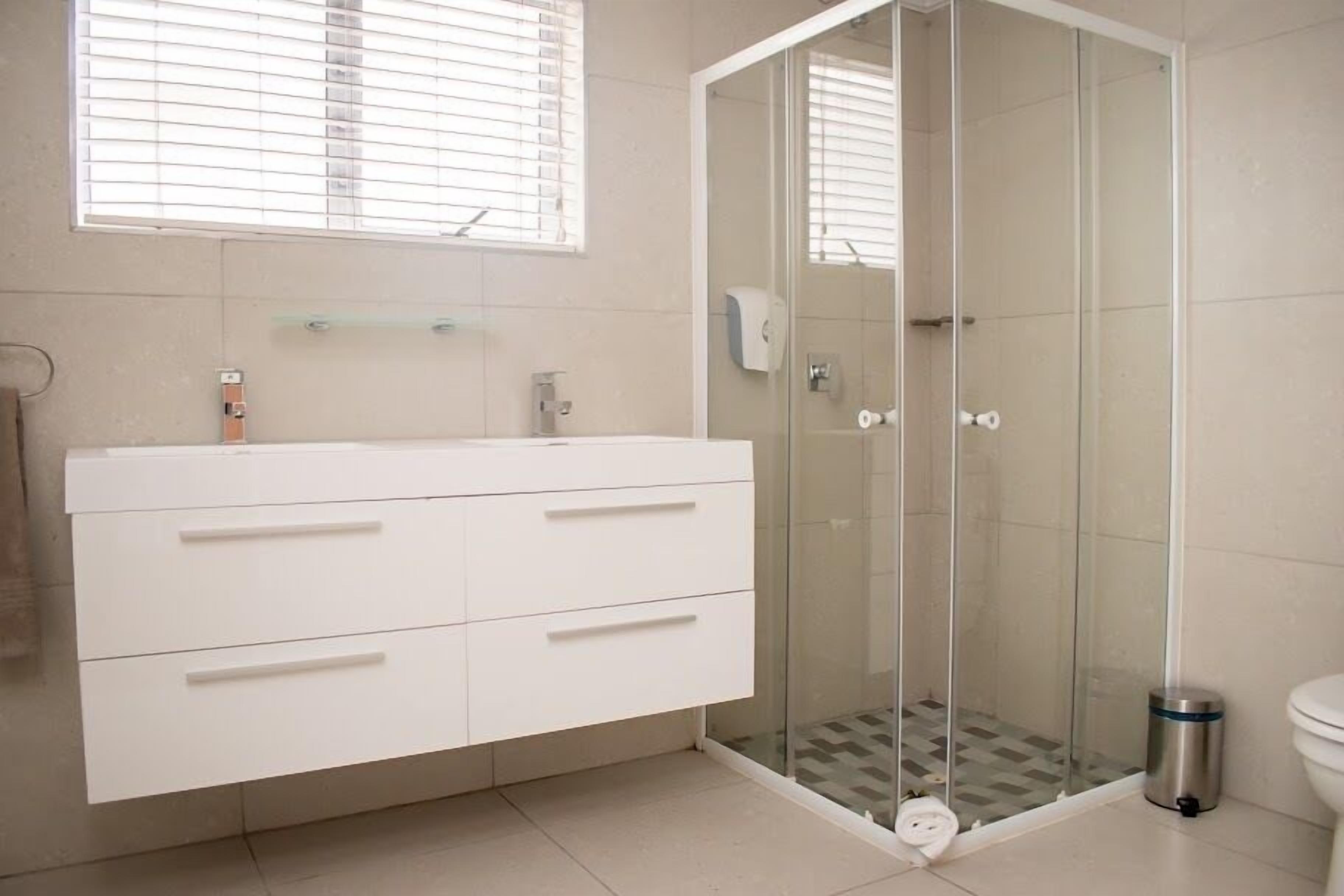 A bathroom with a white vanity, a glass shower enclosure, and a toilet.
