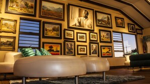 Una sala de estar con techo alto, varias obras de arte enmarcadas en las paredes, un sofá blanco y un sillón verde.