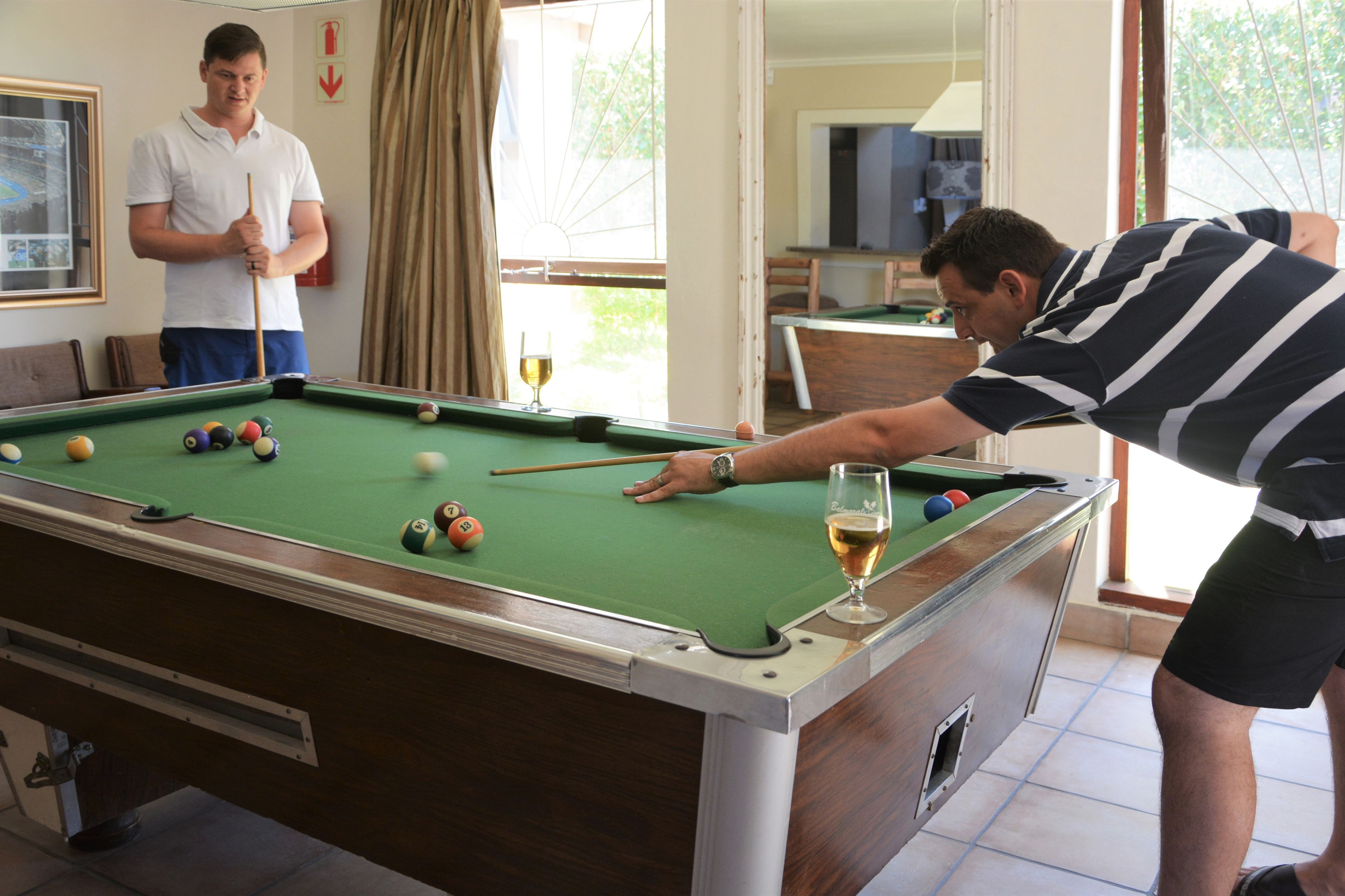 A pool table with balls, a glass of wine, and two people playing.
