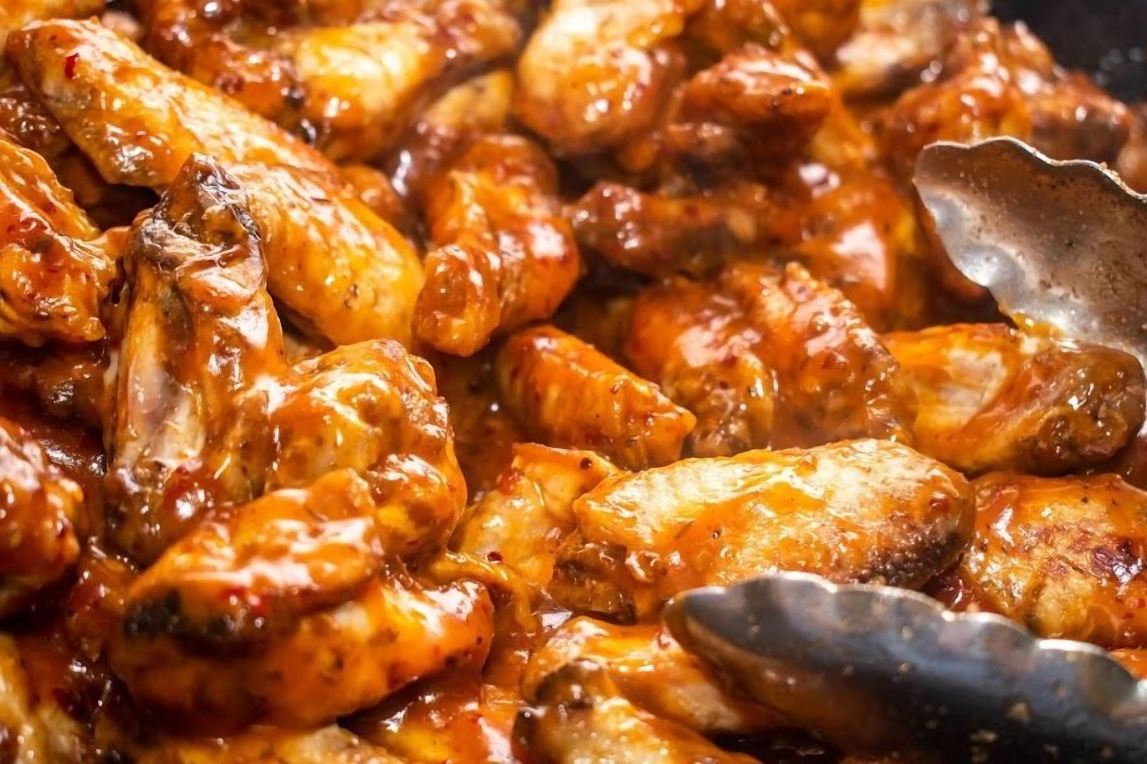 A close-up of a dish with chicken wings coated in a glossy, reddish sauce.