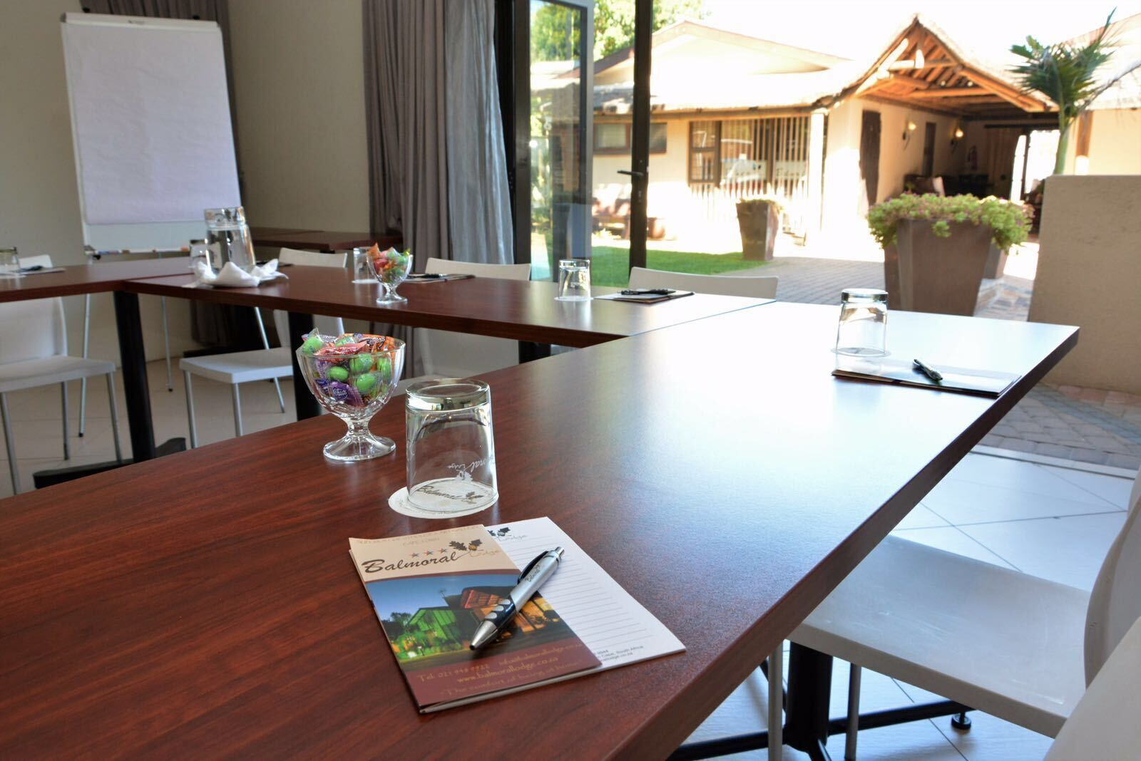 A conference table with a glass bowl of candies, a glass of water, and a pen on a brochure.