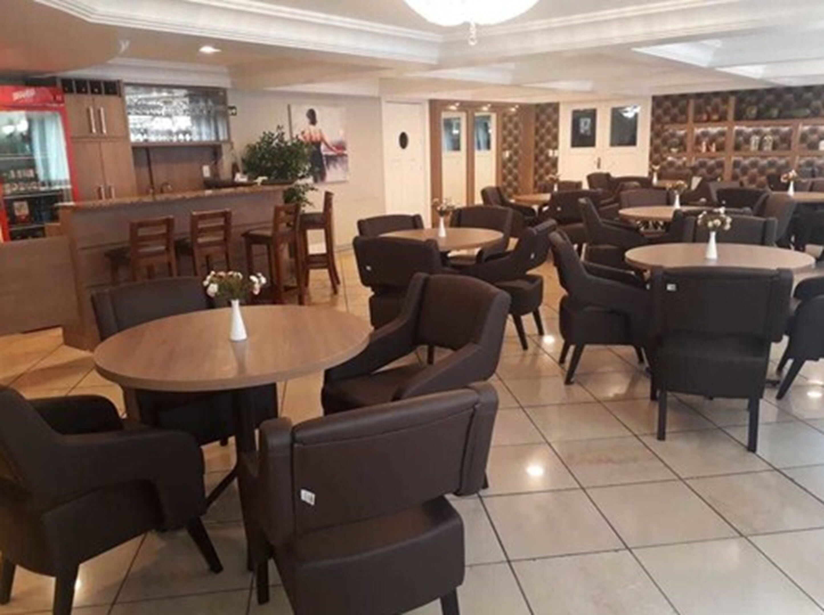 Un ristorante con tavoli rotondi e sedie scure, un'area bar con un bancone e una parete decorata con quadri.