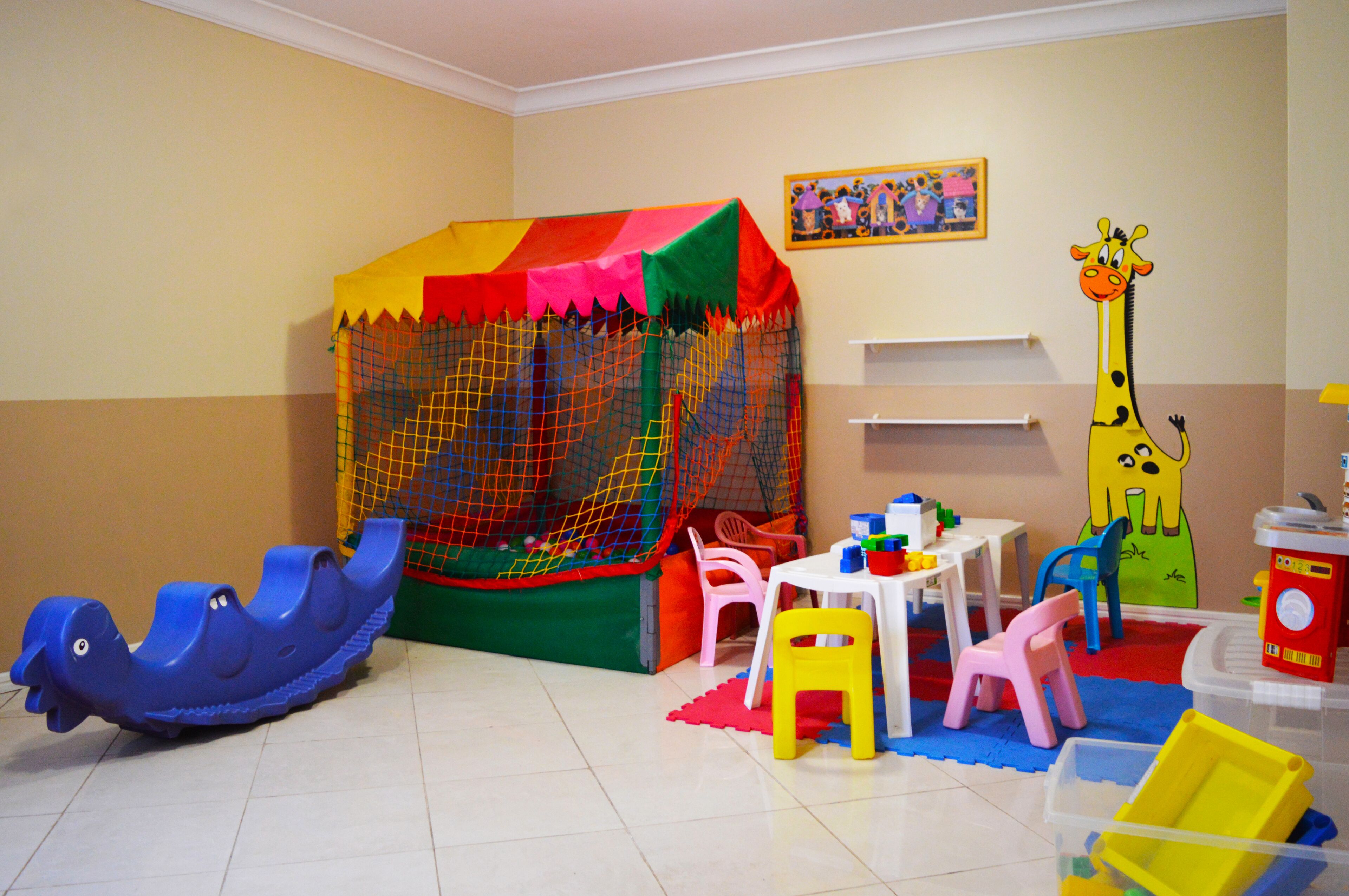 A play area with a colorful play tent, a blue slide, and a giraffe decoration.