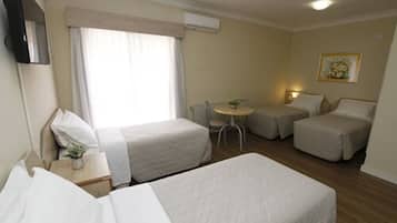 Quarto de hotel com duas camas de solteiro, uma mesa pequena, uma cadeira e uma janela com cortinas.