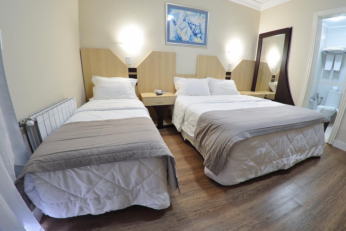 A hotel room with two beds, a bedside table with a phone, a wall-mounted light, and a bathroom visible through an open door.