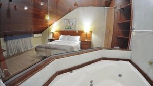 Quarto com cama grande, teto de madeira, banheira branca e guarda-roupa de madeira.