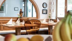 A dining area with a wooden table, chairs, and a statue. - Hotel Christina (Seefeld in Tirol)