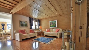 A spacious living room with wooden ceilings, two sofas with red cushions, a blue rug, and a wooden cabinet with glass lanterns. - Hotel Christina (Seefeld in Tirol)