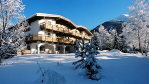 A snow-covered building with multiple balconies, surrounded by snow-laden trees and a mountain in the background. - Hotel Christina (Seefeld in Tirol)