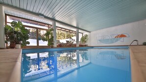 An indoor swimming pool with clear windows, potted plants, and a logo on the wall. - Hotel Christina (Seefeld in Tirol)