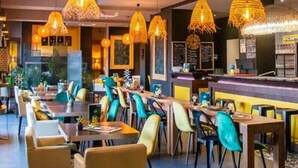 A restaurant interior with multiple tables and chairs, hanging pendant lights, and a counter area. - Safari Hotel (Carpentras)