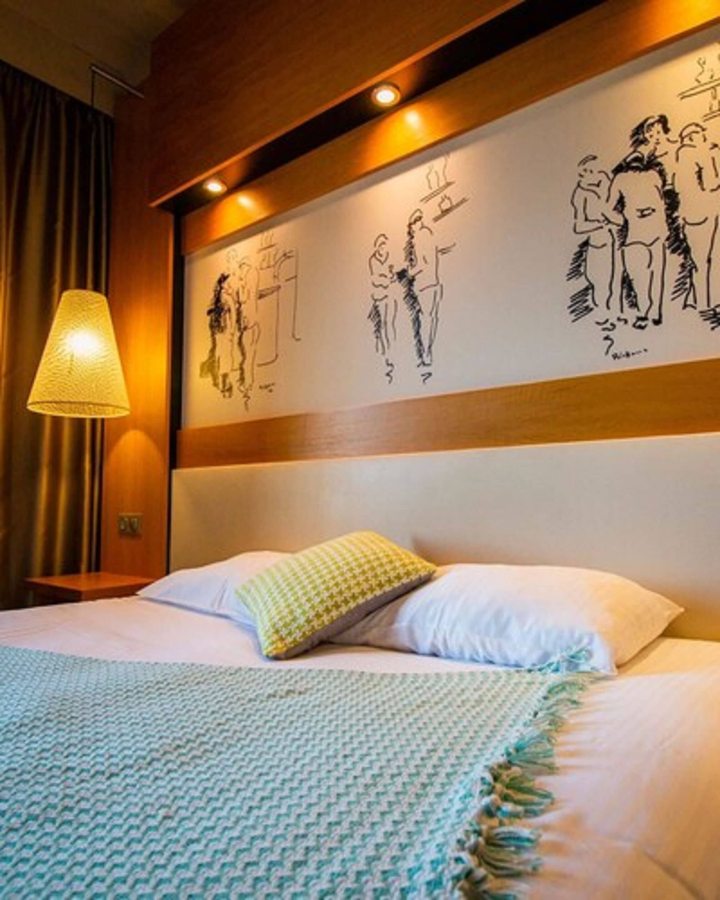 A hotel room with a bed, a lamp, and a wall with artwork.