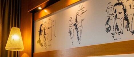 Una habitación de hotel con una cama, una lámpara y una pared decorada con obras de arte.