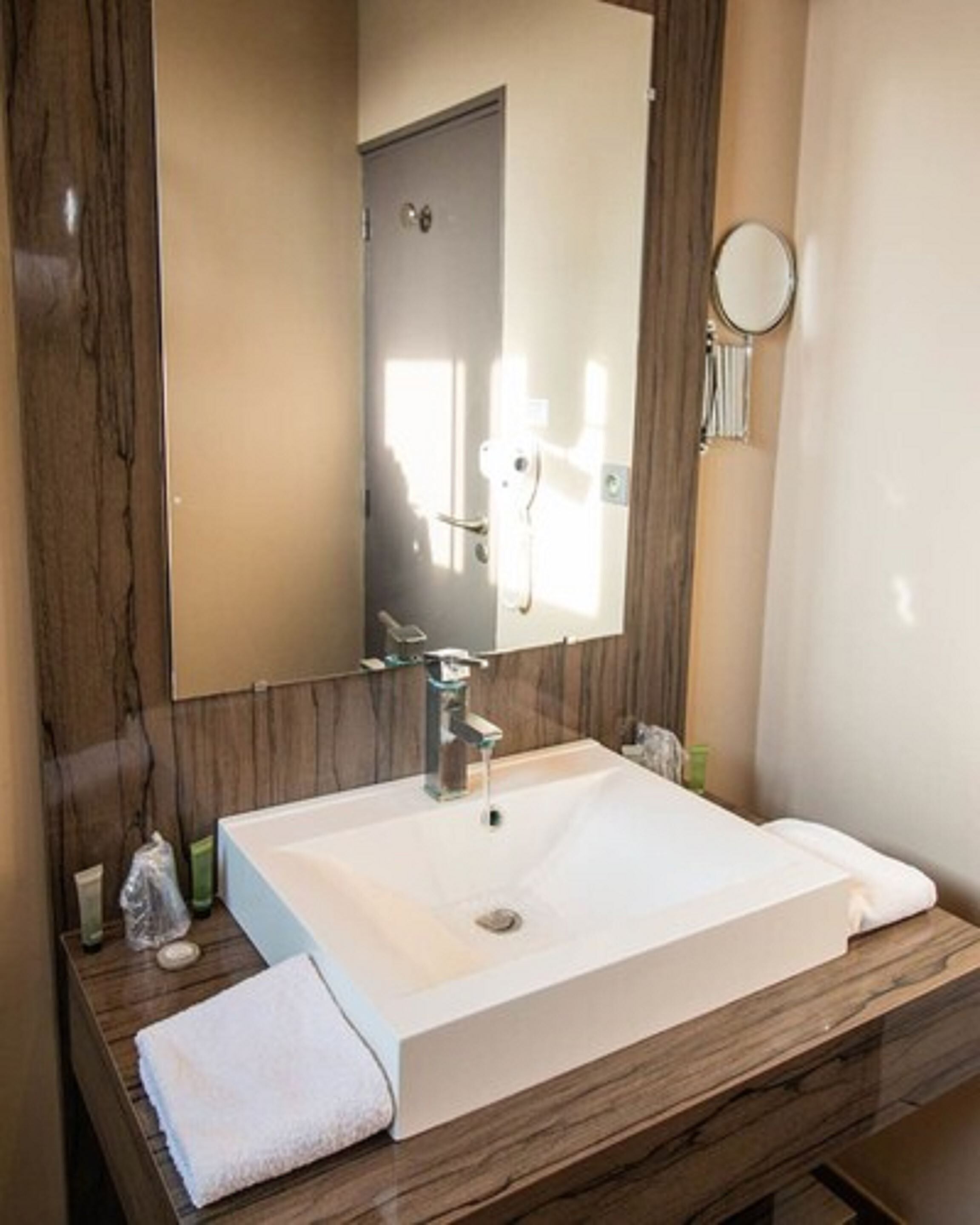Un baño con un espejo grande, un lavamanos blanco y un mueble de tocador de madera.