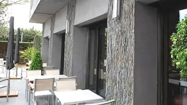 An outdoor seating area with tables and chairs, a stone wall, and a glass door leading to the interior. - Safari Hotel (Carpentras)