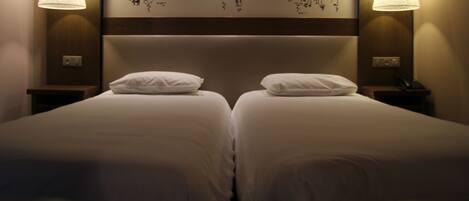 Ein Hotelzimmer mit zwei Betten, einem Kopfteil mit Wandkunst und Nachttischlampen.