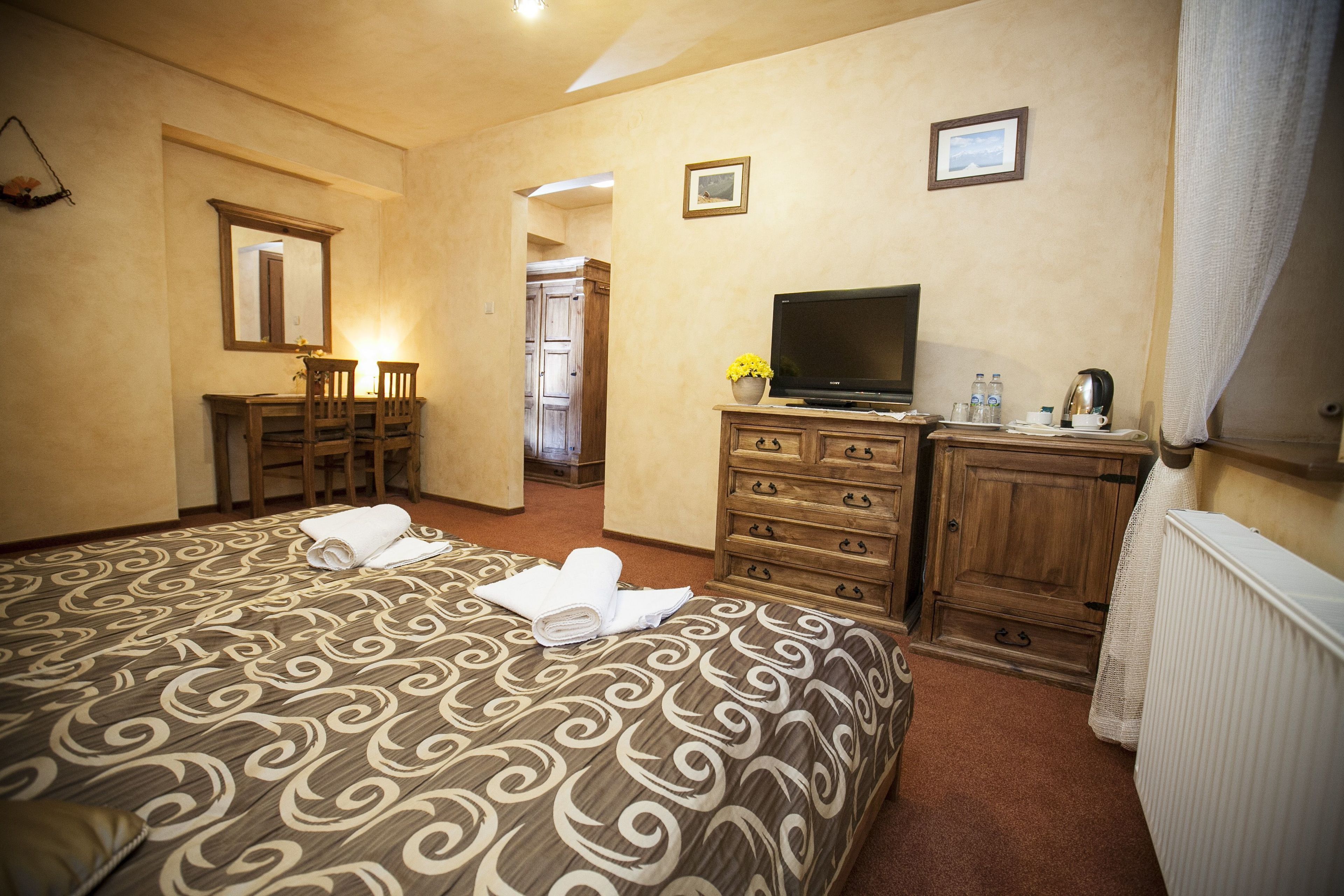 A hotel room with a large bed, a TV, a dresser, and a desk with a chair.