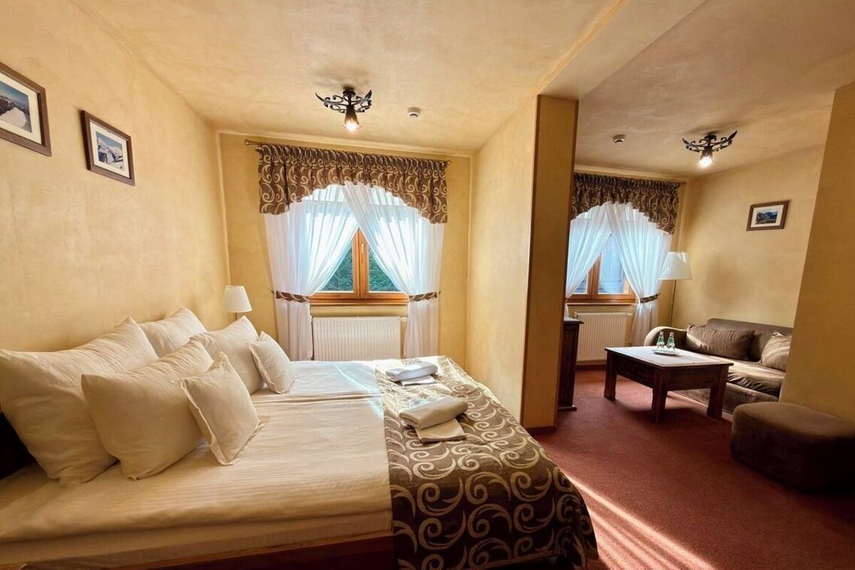A hotel room with a bed, a sofa, a small table, and a window with curtains.