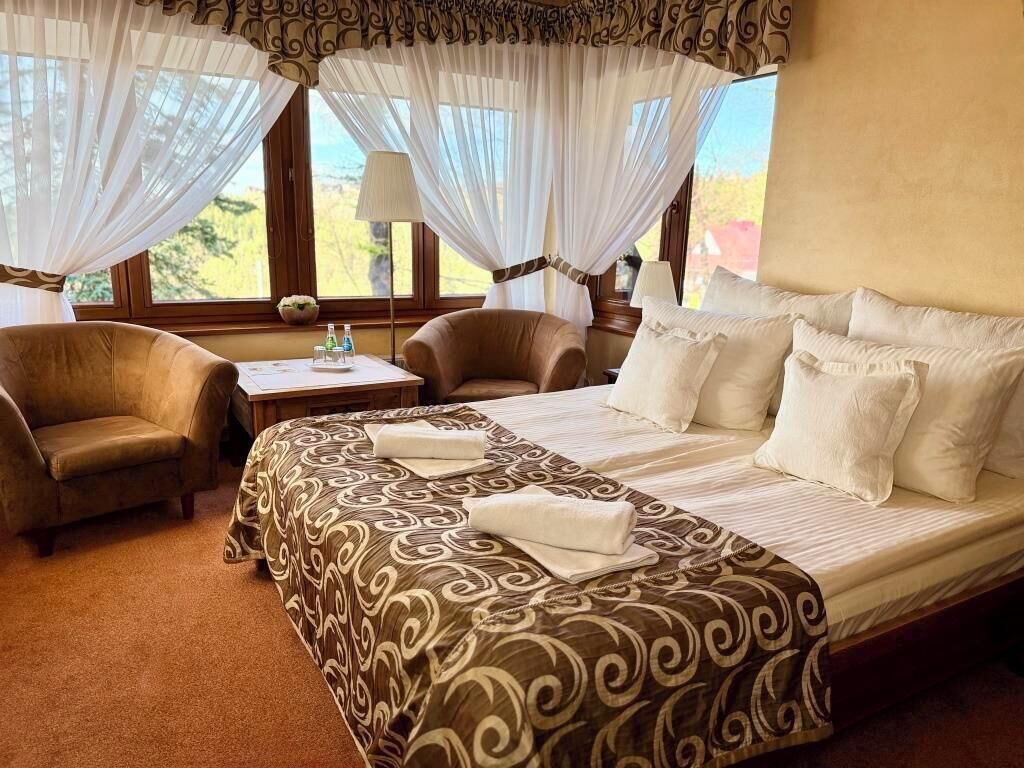 A hotel room with a bed, two chairs, a table with a lamp, and a view of the outdoors.