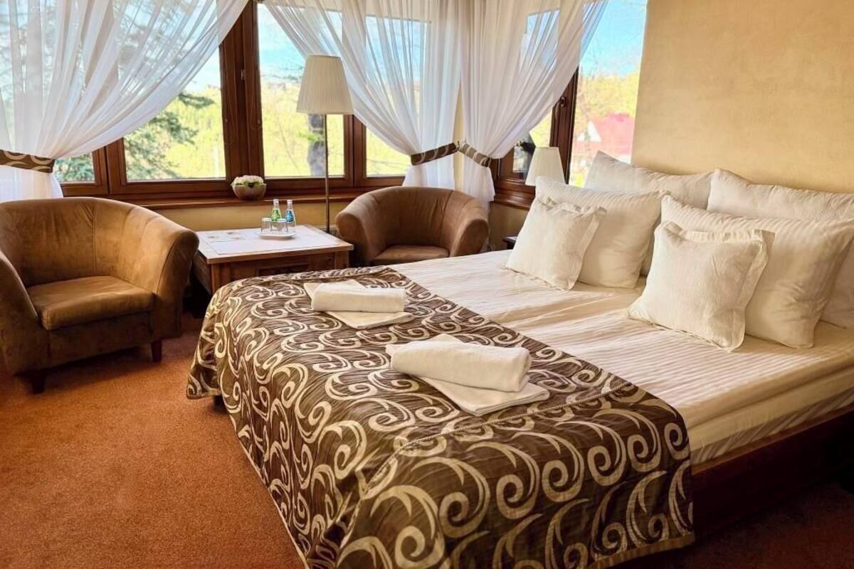 A hotel room with a bed, two chairs, a table with a lamp, and a view of the outdoors.