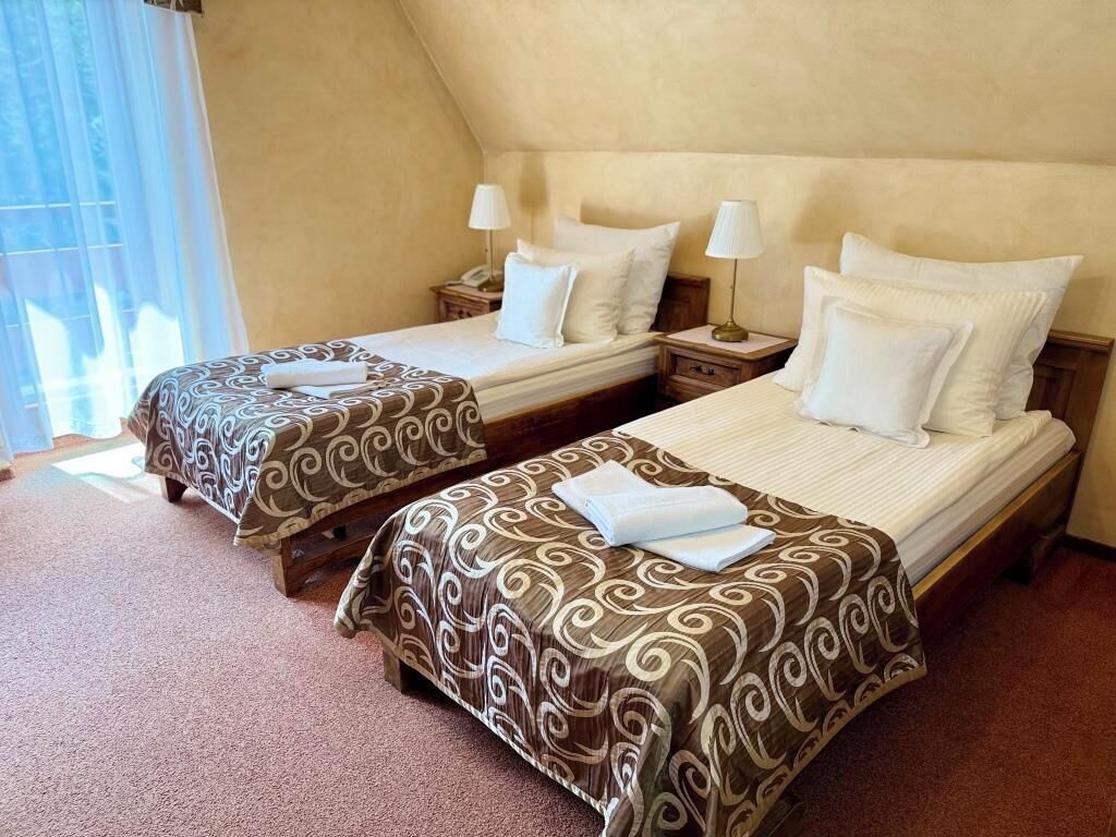 Two twin beds with patterned bedspreads, bedside lamps, and a window with curtains.