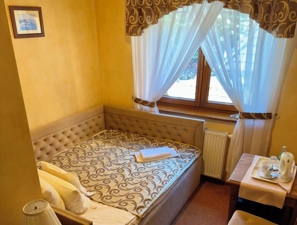 A small, neatly arranged bedroom with a single bed, a bedside table with a tray, and a window with curtains.