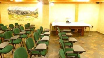 Une salle de conférence avec des chaises et des tables vertes, un grand tableau au mur et une table en bois recouverte d’une nappe blanche.