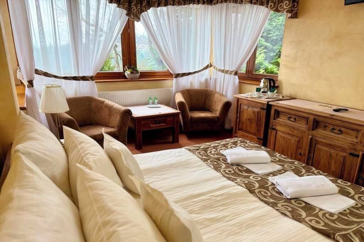 A hotel room with a bed, two armchairs, a wooden desk, and a window with curtains.