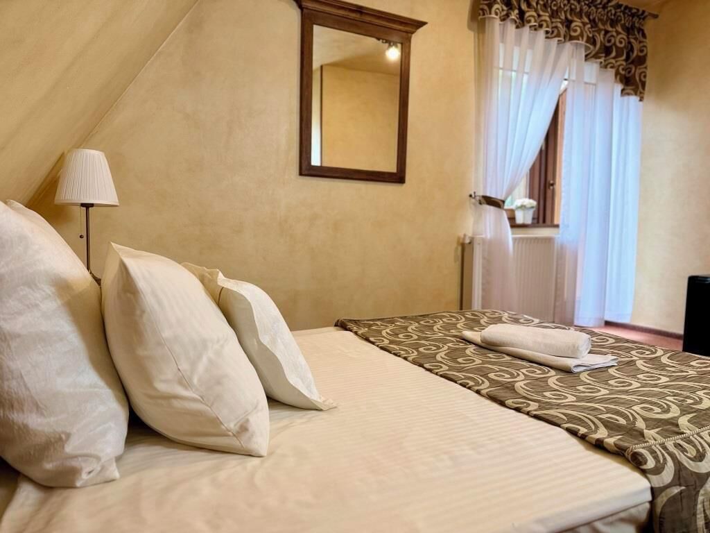 A bedroom with a bed, pillows, a lamp, a mirror, and a window with curtains.