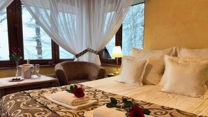 A hotel room with a large bed, a chair, a bedside table with a lamp, and a window with curtains. - Dwór Karolówka (Zakopane)