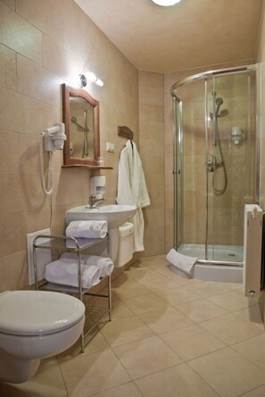 A bathroom with a toilet, sink, glass shower enclosure, and a towel rack with towels. - Dwór Karolówka (Zakopane)