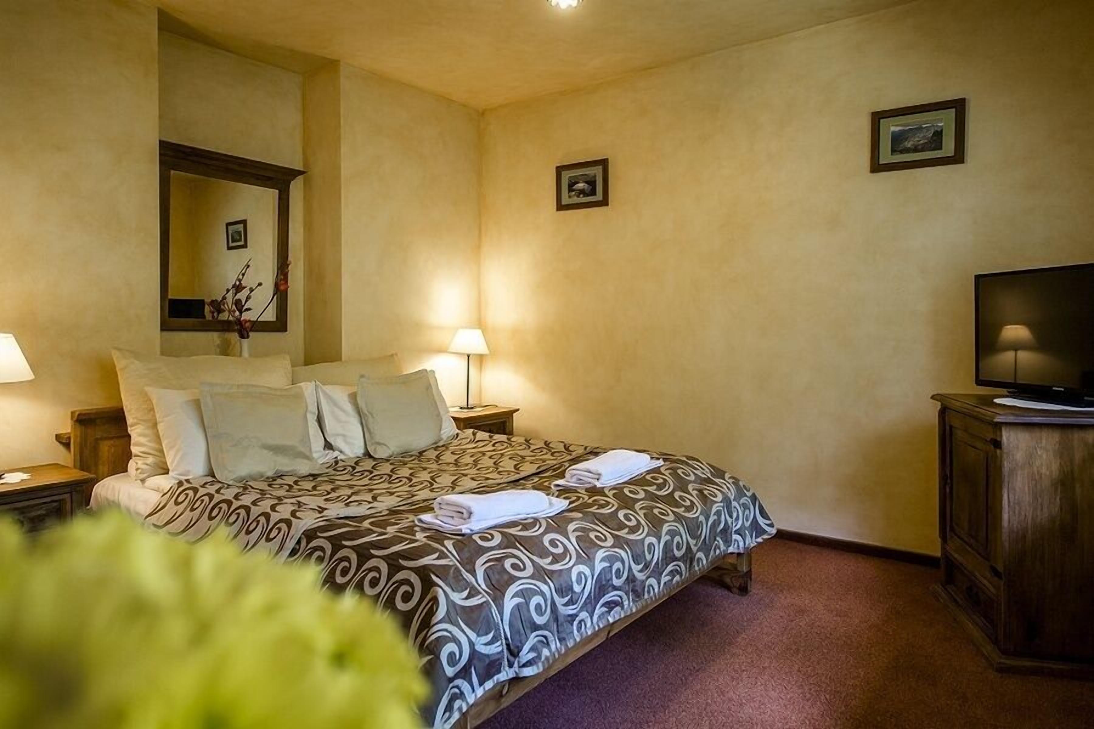 Una habitación de hotel con cama, dos lámparas de noche, televisión y espejo.