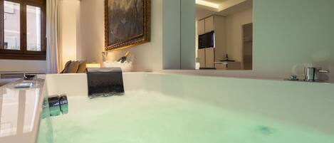 A modern bathroom with a large bathtub, a mirror, a sink, and a television.