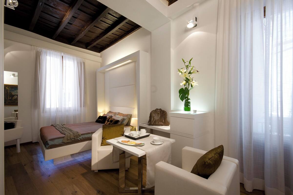 Un dormitorio moderno con cama, mesita de noche y una pequeña zona de estar con sillón y mesa.