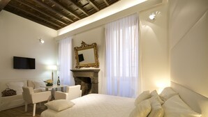 Een slaapkamer met een groot bed, een open haard, een televisie en een zithoek met een tafel en stoelen.