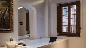 Een moderne badkamer met een groot bad, een spiegel en een raam met houten luiken.