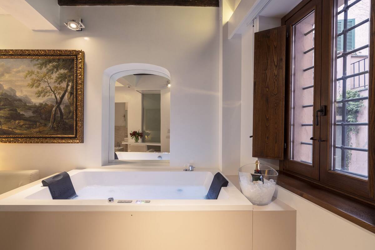 Un baño moderno con una bañera grande, un espejo y una ventana con contraventanas de madera.
