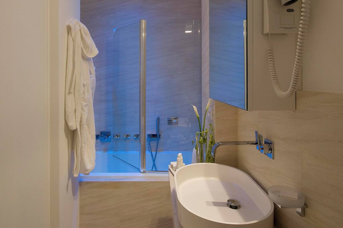Un baño moderno con ducha envuelta en vidrio, un lavamanos blanco y un secador de pelo fijado en la pared.