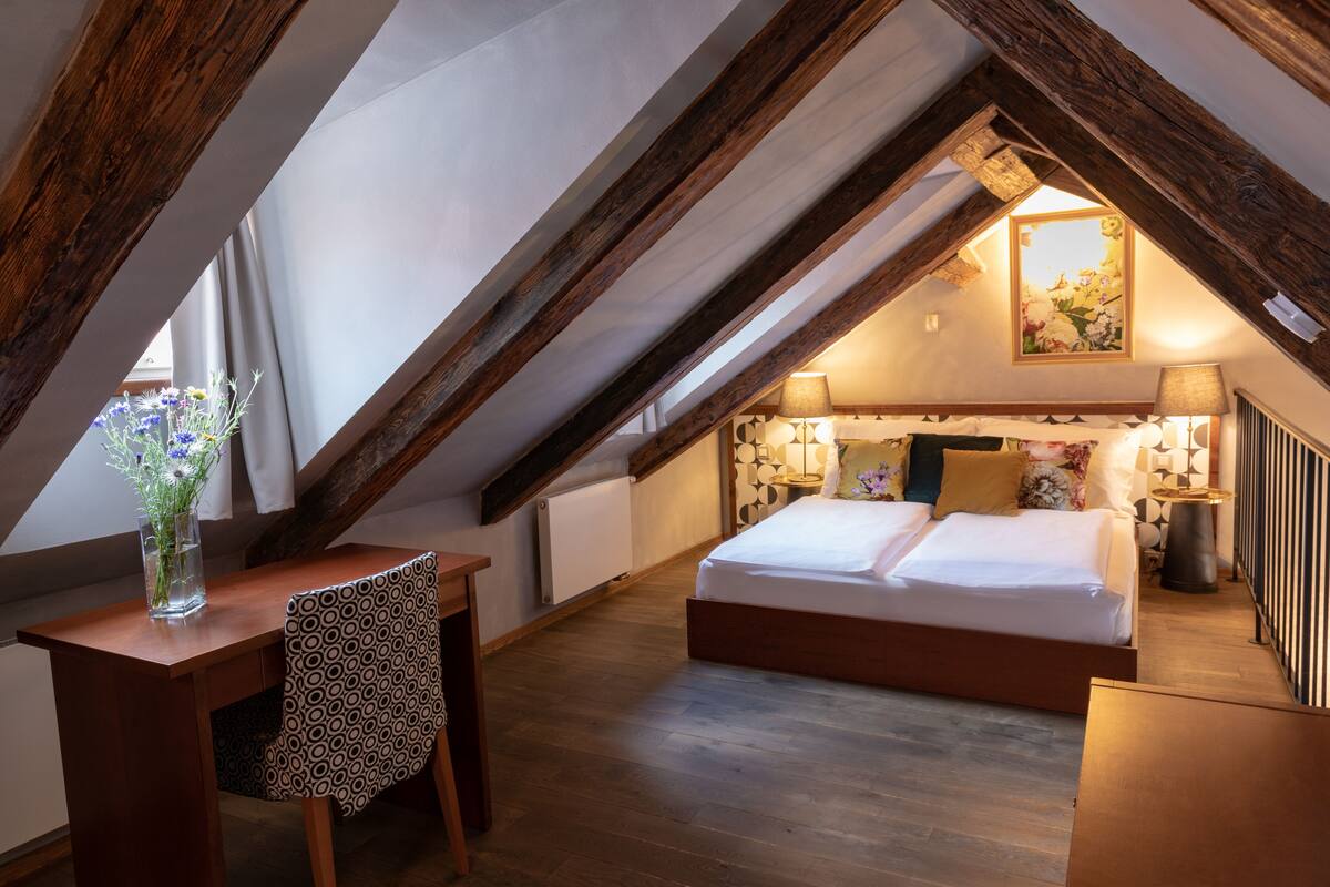 A bedroom with a wooden ceiling, a bed, a desk, and a chair.