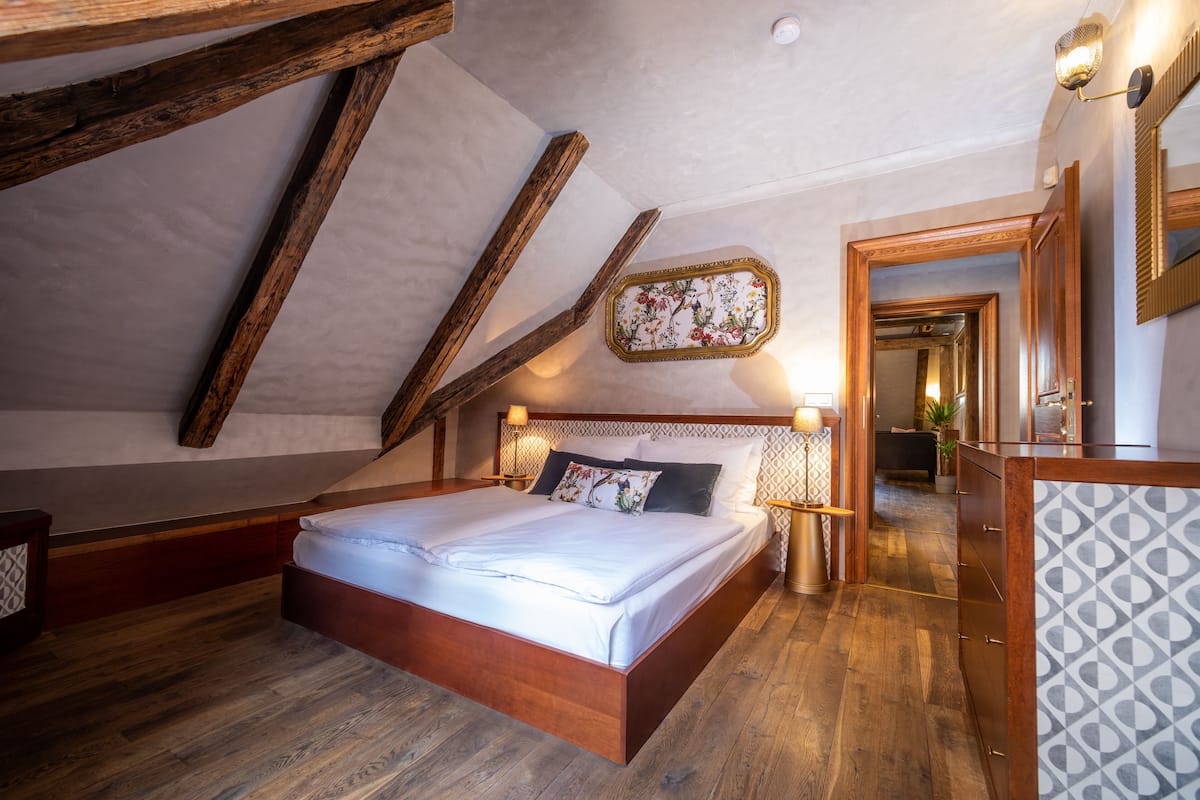 A bedroom with a wooden bed, a nightstand, a mirror, and a patterned wall.