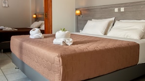 Un letto rifatto con cura, con una coperta rosa, cuscini bianchi e due asciugamani bianchi con una foglia verde sopra.