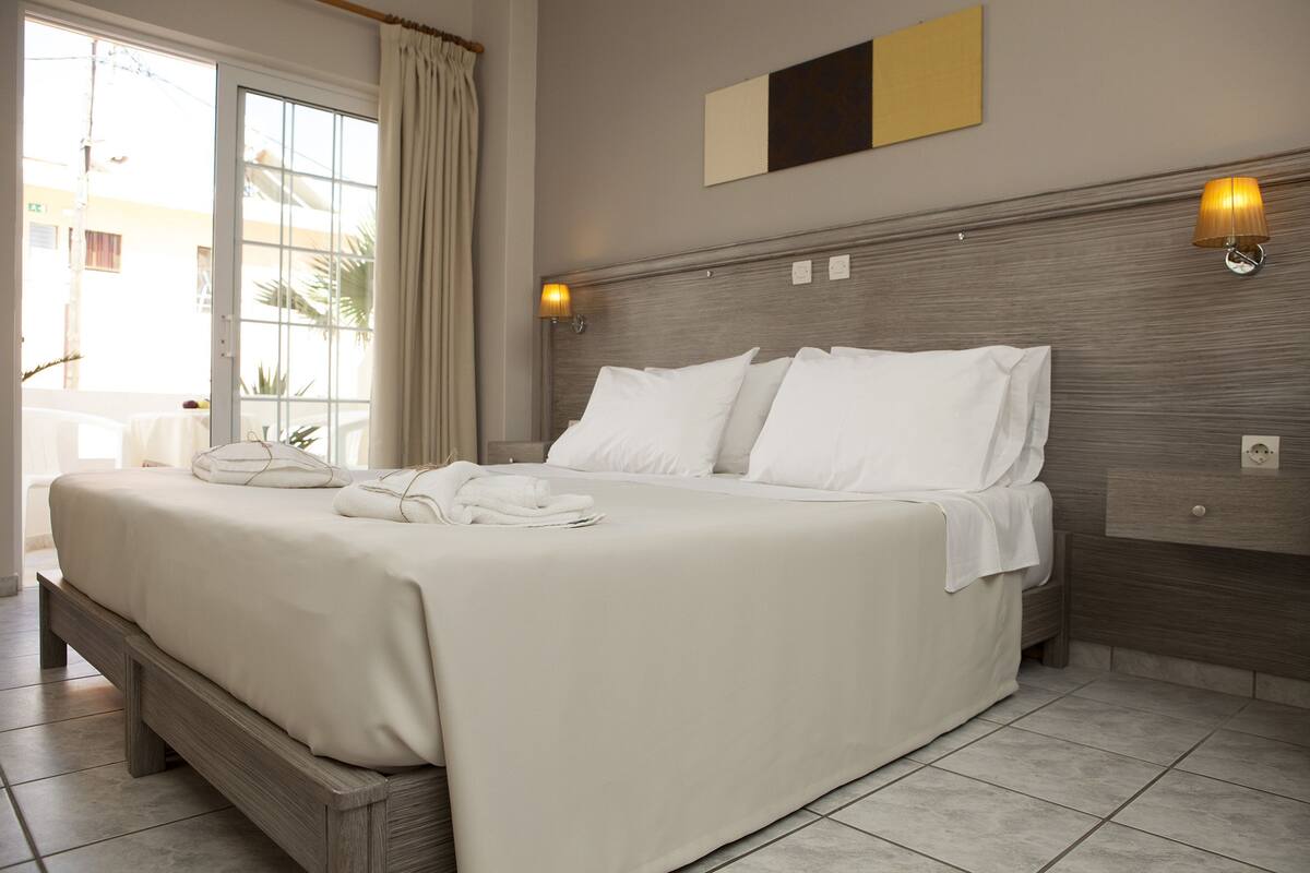 Una cama bien hecha con sábanas blancas, cabecera de madera y dos lámparas fijadas a la pared.