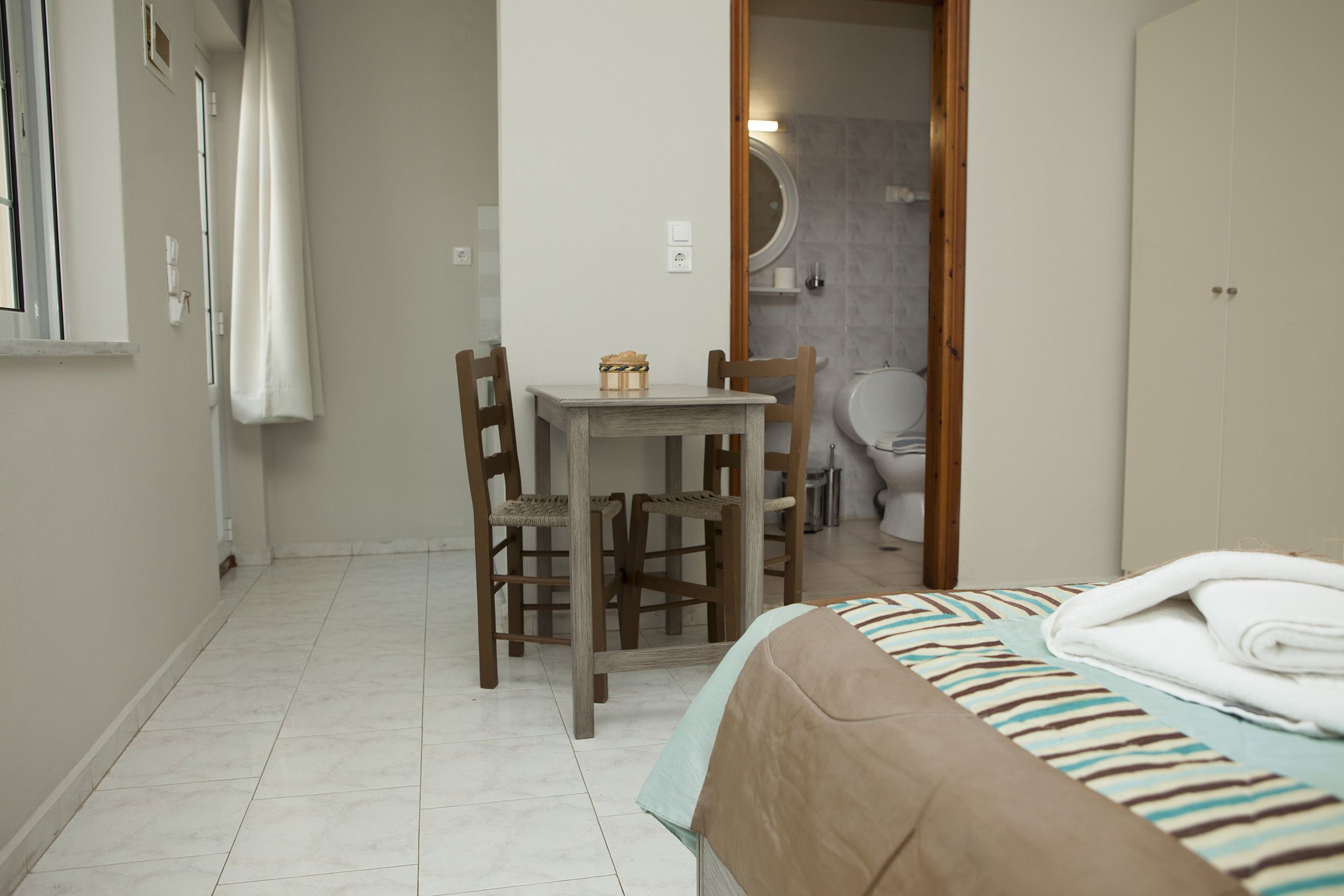 A small, clean room with a bed, a table, and two chairs. A bathroom is visible through an open door.