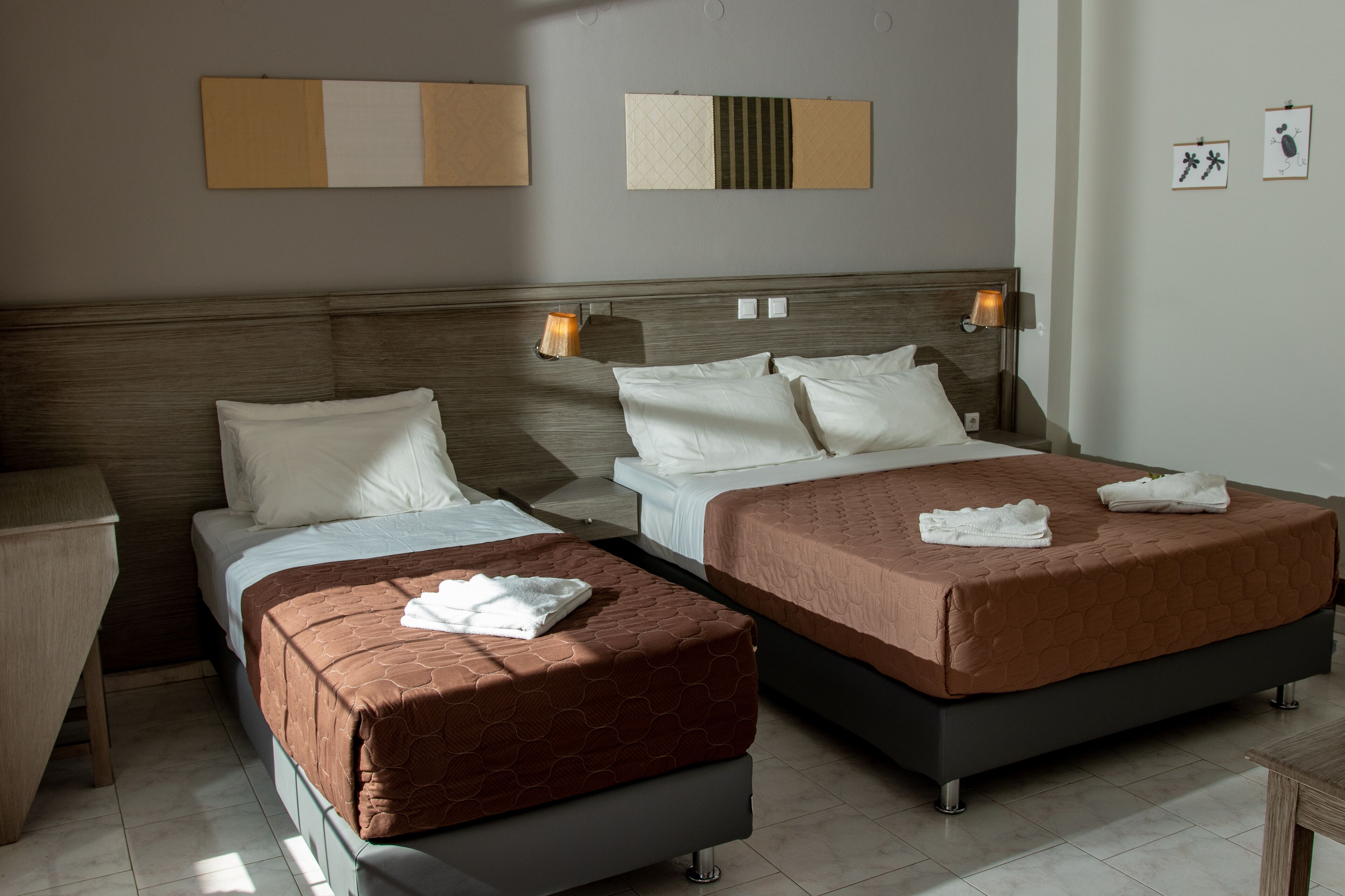 Ein Hotelzimmer mit zwei Betten, einem hölzernen Kopfteil, Nachttischlampen und einem kleinen Tisch.