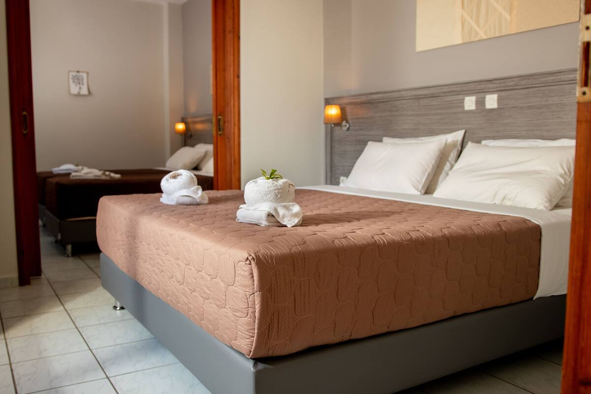 Una cama bien hecha con colcha marrón, cabecera de madera y dos lámparas de noche.